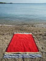 Beach towel in red color with two extra panels of striped cotton fabric on its sides and cotton fringes